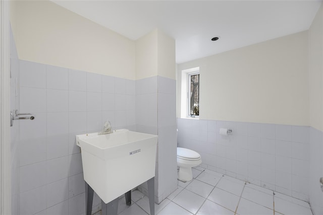 bathroom with toilet, a sink, wainscoting, tile walls, and tile patterned floors