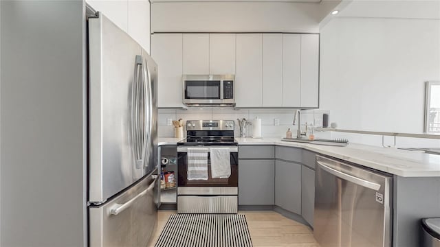 1043 Halsey St Unit 4, Brooklyn, NY 11207 - kitchen featuring stainless steel appliances, a peninsula, decorative backsplash, light wood-type flooring, and gray cabinetry