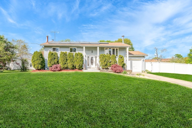 split foyer home featuring a garage, fence, roof mounted solar panels, a front lawn, and concrete driveway