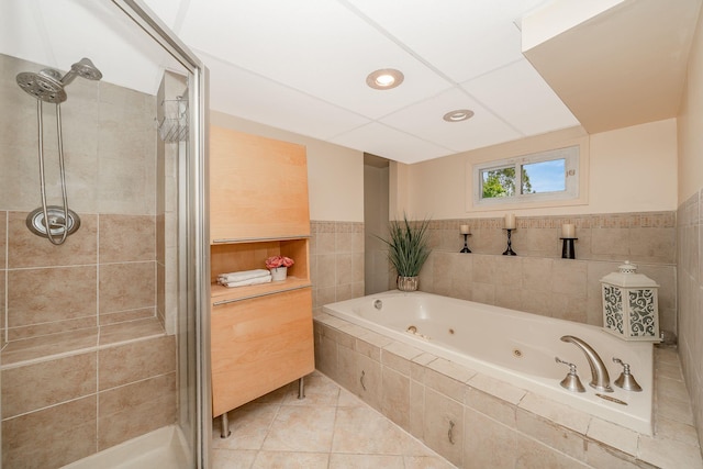 full bath featuring tile walls, a tub with jets, a wainscoted wall, tile patterned floors, and a shower stall