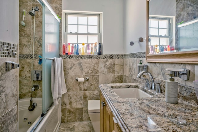 bathroom with tile walls, shower / bath combination with glass door, toilet, and vanity