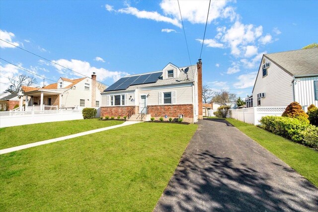 bungalow-style home featuring a front lawn, driveway, roof mounted solar panels, fence, and brick siding