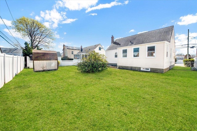 back of house featuring a lawn, a fenced backyard, an outdoor structure, and a shed