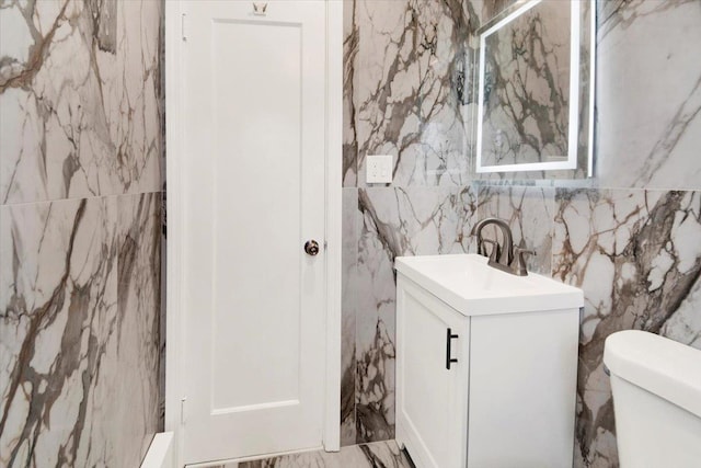 bathroom featuring marble finish floor, tile walls, toilet, and vanity