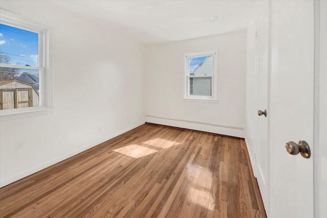 spare room with baseboards, wood finished floors, a wealth of natural light, and a baseboard radiator