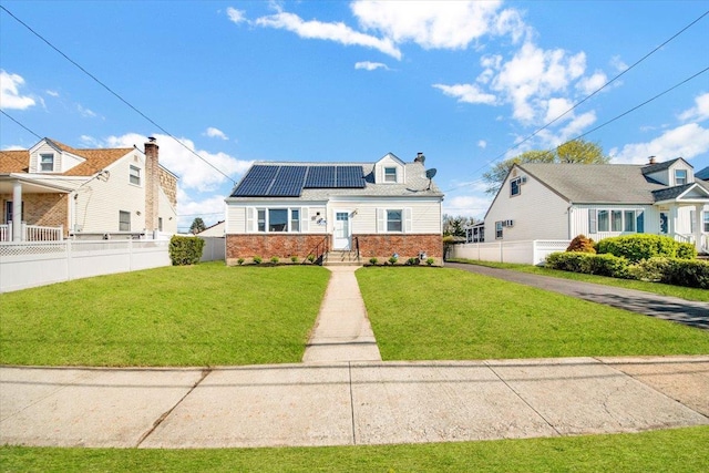 bungalow-style home featuring a chimney, fence private yard, roof mounted solar panels, a front yard, and brick siding