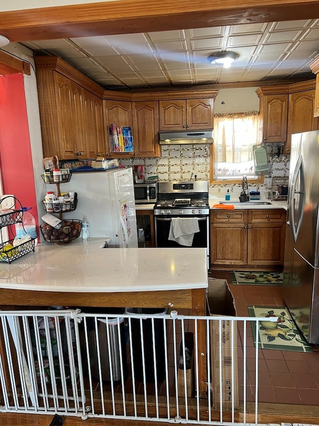 216 N Ocean Ave, Freeport, NY 11520 - kitchen with appliances with stainless steel finishes, light countertops, under cabinet range hood, a peninsula, and brown cabinetry