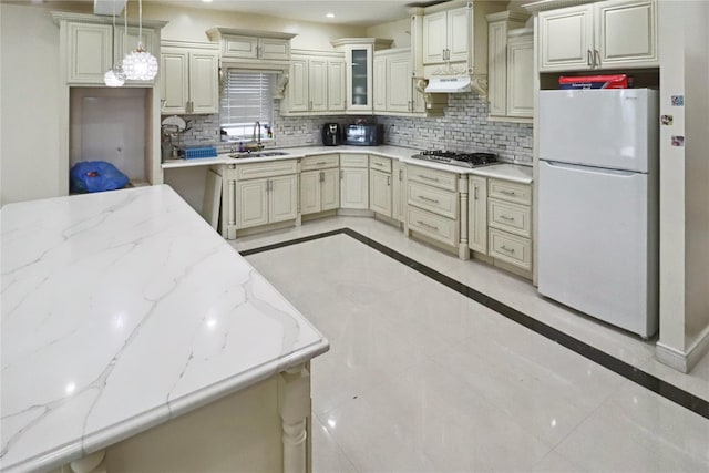 kitchen with freestanding refrigerator, under cabinet range hood, decorative backsplash, stainless steel gas stovetop, and a sink