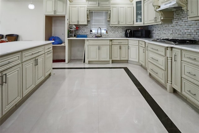 kitchen with tasteful backsplash, a sink, light countertops, under cabinet range hood, and stainless steel gas cooktop