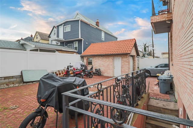 back of property featuring a tiled roof, fence, an outdoor structure, a patio, and brick siding