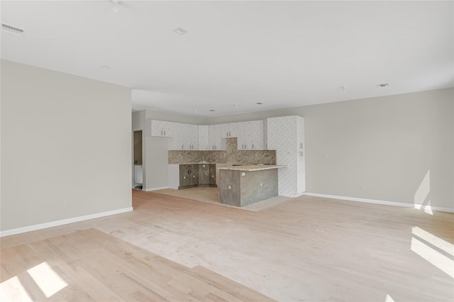unfurnished living room with visible vents, light wood-style flooring, and baseboards