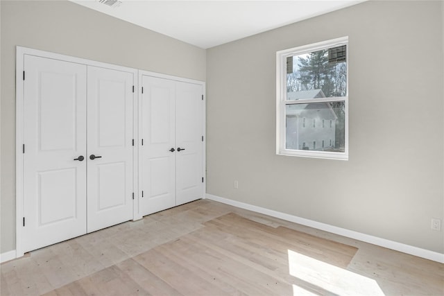 unfurnished bedroom with visible vents, two closets, wood finished floors, and baseboards