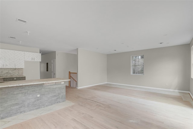 unfurnished living room featuring visible vents, light wood-style flooring, and baseboards
