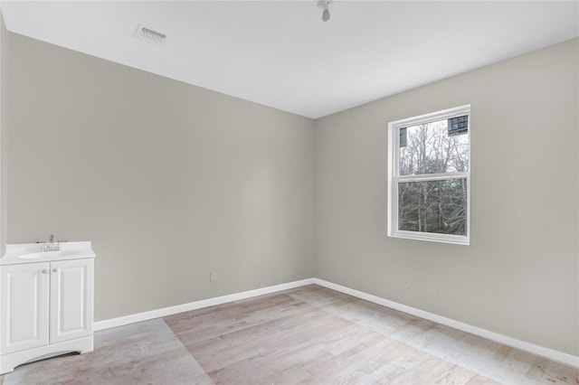 empty room with visible vents, baseboards, light wood-style flooring, and a sink