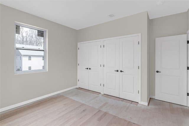 unfurnished bedroom featuring visible vents, light wood-type flooring, two closets, and baseboards