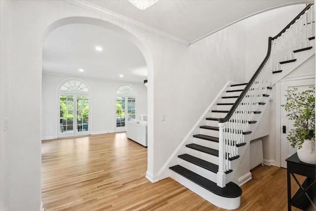 stairs with arched walkways, wood finished floors, radiator heating unit, recessed lighting, and baseboards