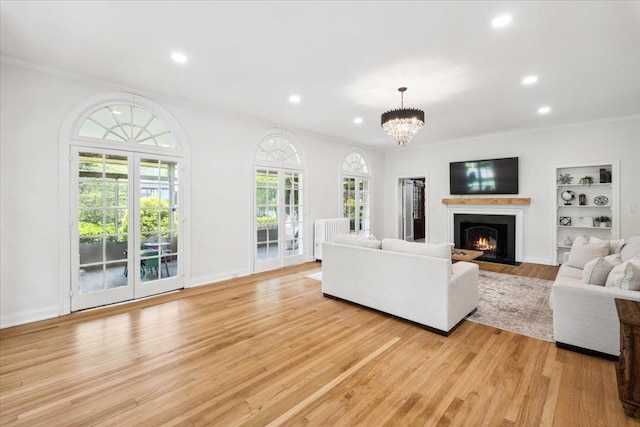 living room featuring ornamental molding, light wood-style flooring, a fireplace with flush hearth, a chandelier, and recessed lighting