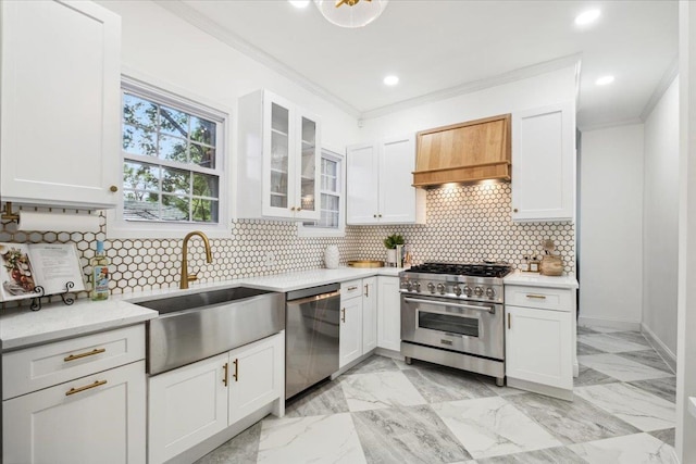 kitchen with stainless steel appliances, a sink, premium range hood, crown molding, and white cabinets