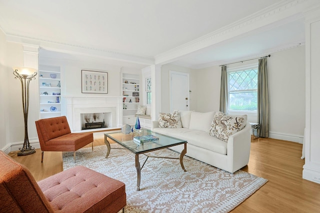 living room with light wood-style flooring, baseboards, a fireplace with raised hearth, ornamental molding, and built in shelves