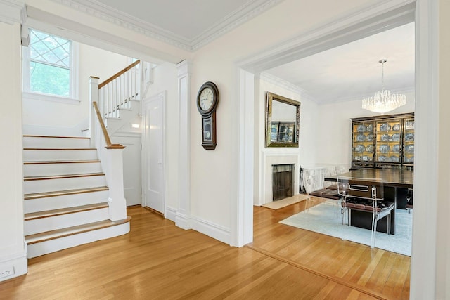 foyer with wood finished floors, stairway, crown molding, a fireplace with flush hearth, and a chandelier
