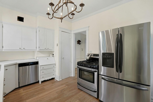 kitchen with appliances with stainless steel finishes, ornamental molding, white cabinets, light wood finished floors, and a chandelier
