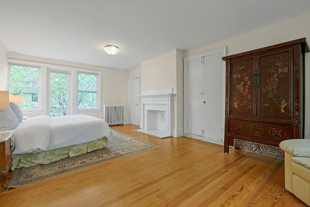 bedroom featuring radiator, light wood-style floors, and a fireplace