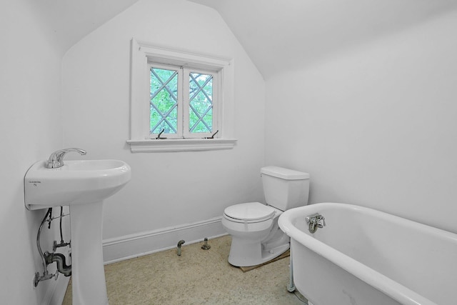 bathroom with a soaking tub, vaulted ceiling, toilet, baseboards, and a sink