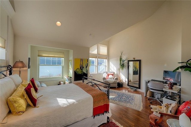bedroom with high vaulted ceiling and wood finished floors