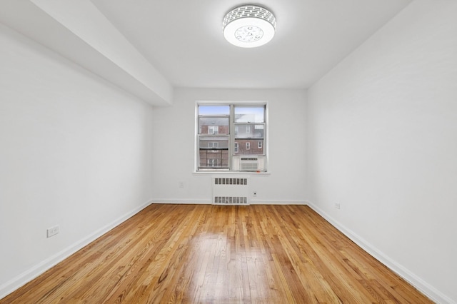 empty room with radiator heating unit, hardwood / wood-style floors, and baseboards