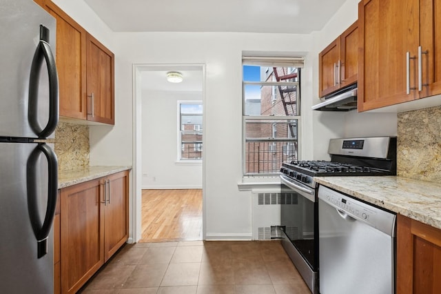 kitchen featuring brown cabinetry, tasteful backsplash, under cabinet range hood, and stainless steel appliances