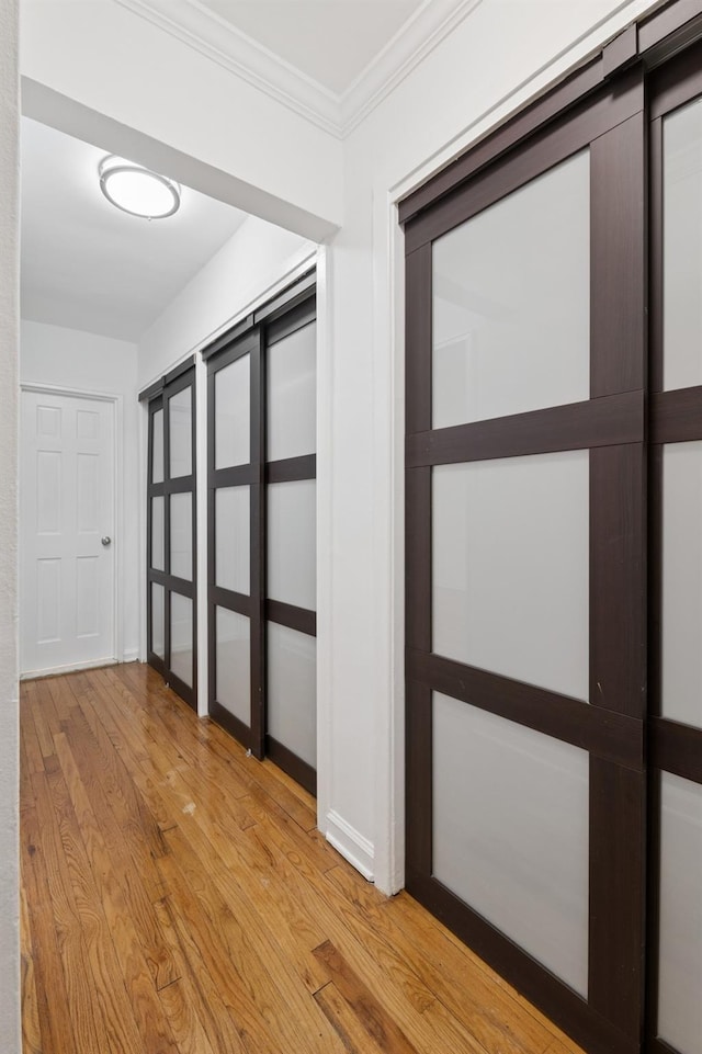 hallway featuring baseboards, light wood-type flooring, and ornamental molding