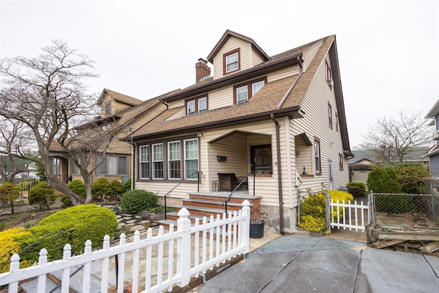 view of front facade featuring a porch, a shingled roof, a gate, and a fenced front yard
