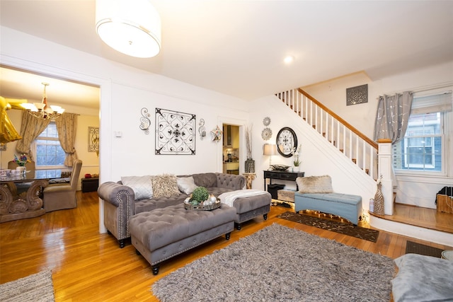 living room with light wood-style floors, a notable chandelier, a wealth of natural light, and stairway