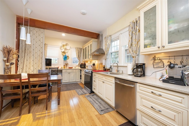 kitchen featuring wall chimney range hood, light wood-style floors, decorative backsplash, stainless steel dishwasher, and a sink