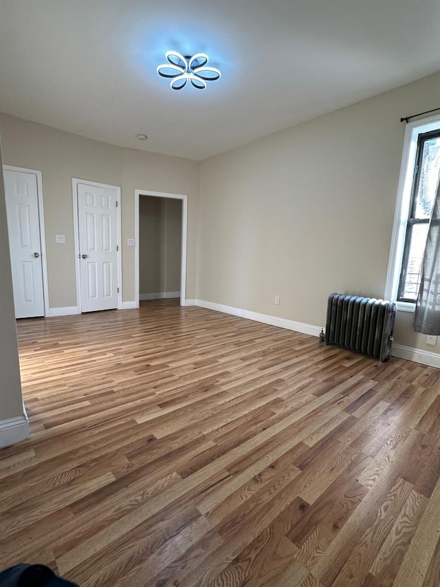unfurnished room featuring baseboards, radiator, and wood finished floors