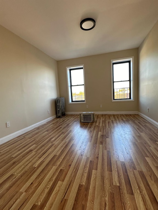 spare room featuring an AC wall unit, baseboards, and wood finished floors