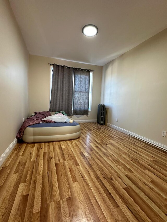 unfurnished bedroom featuring wood finished floors, radiator heating unit, and baseboards