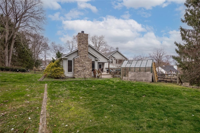 rear view of property with a greenhouse, an outdoor structure, a yard, and a chimney