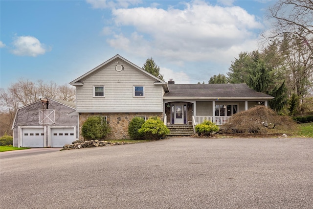 split level home with a chimney, stone siding, an outbuilding, a porch, and a garage