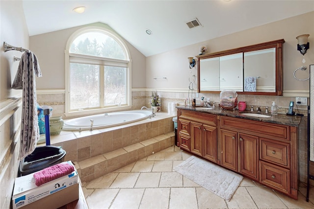 bathroom featuring lofted ceiling, double vanity, visible vents, a sink, and a garden tub