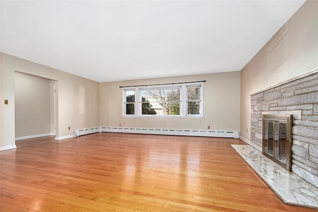 unfurnished living room with a baseboard radiator, baseboards, a stone fireplace, and light wood-type flooring