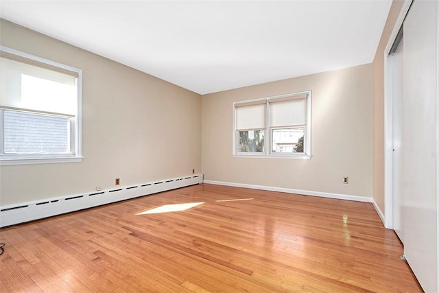 unfurnished room featuring a baseboard heating unit, baseboards, and light wood-style flooring
