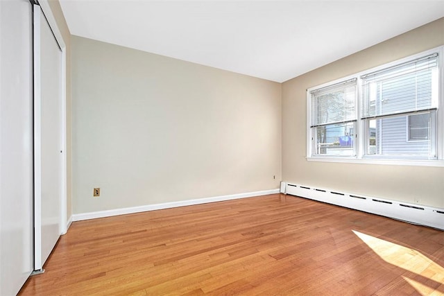 unfurnished bedroom featuring light wood-type flooring, baseboard heating, baseboards, and a closet