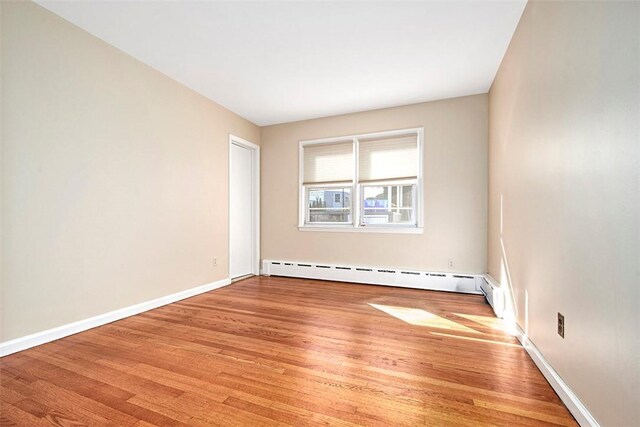 empty room featuring a baseboard heating unit, baseboards, and light wood finished floors