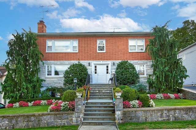 view of front facade with a chimney, brick siding, and stone siding