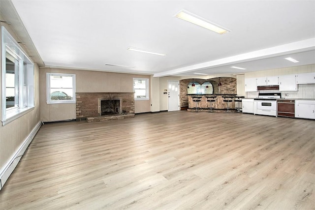unfurnished living room featuring a baseboard radiator, light wood-style flooring, a healthy amount of sunlight, and a fireplace with raised hearth