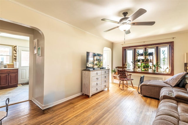 living room featuring crown molding, a wealth of natural light, arched walkways, and light wood-style floors
