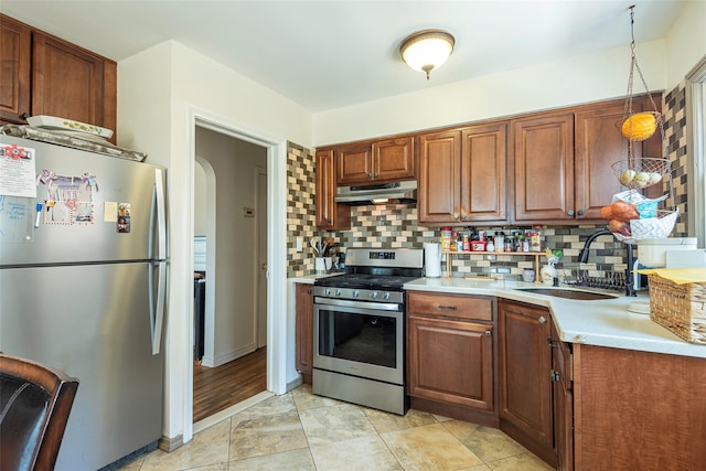 kitchen featuring a sink, light countertops, appliances with stainless steel finishes, under cabinet range hood, and decorative backsplash