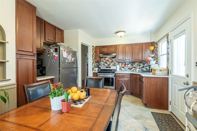 kitchen with tasteful backsplash, a sink, light countertops, appliances with stainless steel finishes, and under cabinet range hood