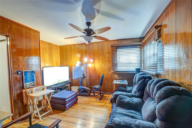 living area with ceiling fan, wood walls, and light wood-style floors